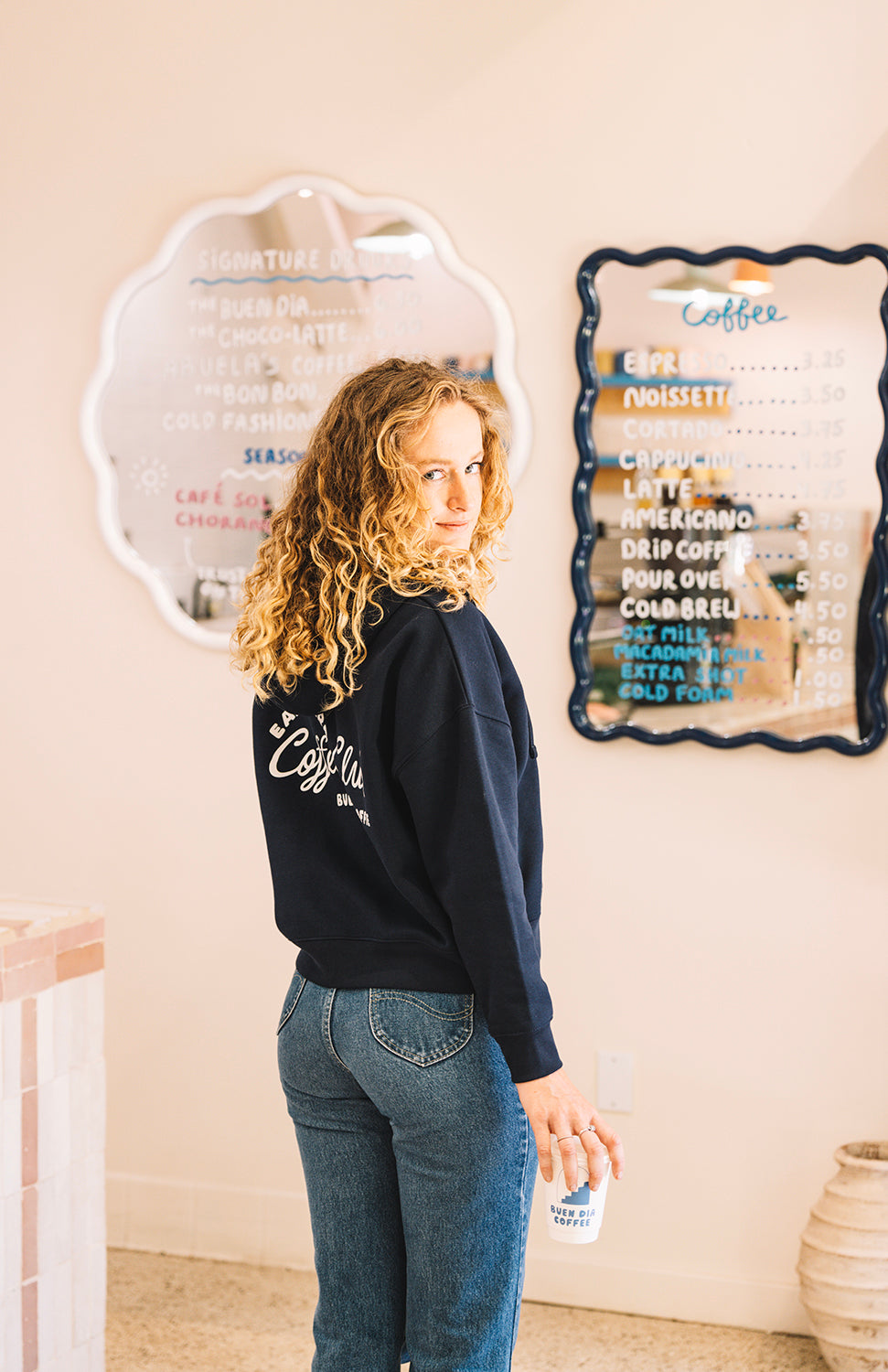Girl wearing Early Bird Coffee Club zip sweatshirt in Buen dia coffee with a cup of coffee