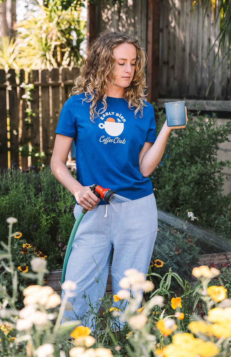Woman gardening with a blue early bird t shirt, drinking a coffee 
Buen dia coffee