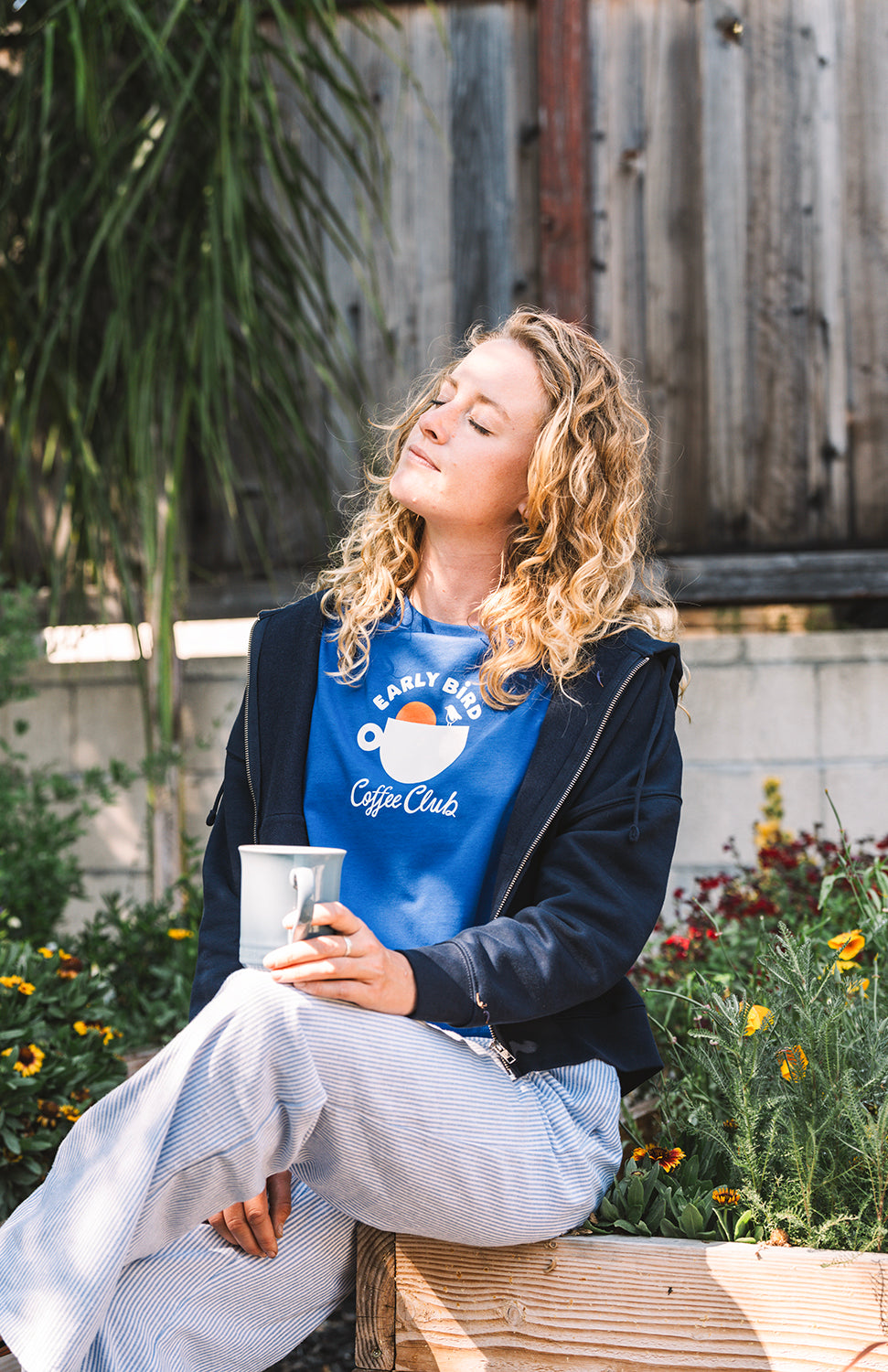 Woman wearing an early bird coffee clun blue t shirt with a coffee cup